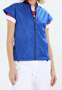 Modrá lehká bunda s krátkými rukávy a předním zipem. Má hladkou texturu a decentní logo detail na rameni.