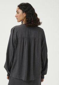 Tummanharmaa pitkähihaista puseroa, jossa on pyöreä pääntie, laskostettu takakappale ja hieman oversized-mitoitus. Pehmeä, tekstuuriainen kangas, jossa on sileä pinta.