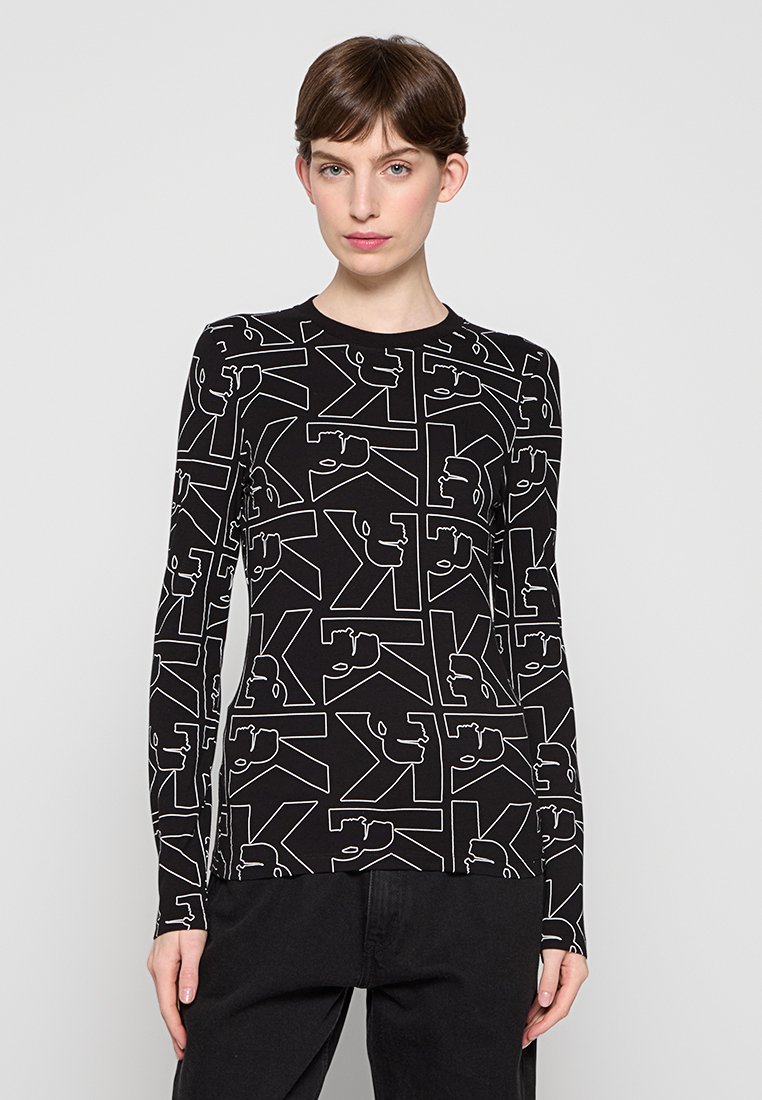 Maglietta nera a maniche lunghe con un motivo geometrico bianco, caratterizzata da forme astratte e contorni. Collo arrotondato, realizzata in tessuto elasticizzato.