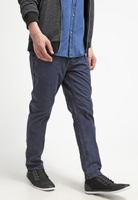 Pantalones ajustados de color navy hechos de algodón con una textura suave y un ligero brillo, combinados con zapatillas altas negras con suelas blancas.