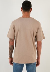 Tricou bej cu mânecă scurtă, cu decolteu rotund, textură netedă și croială lejeră. Prezintă detalii subtile de cusătură pe umăr.