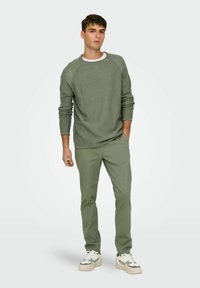 Pull en maille texturée vert clair avec manches raglan, associé à un pantalon slim vert assorti. Des baskets blanches avec des accents verts complètent le look.