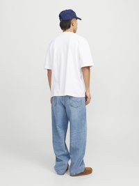 Balta per didelį t-shirt, šviesiai mėlynos plačios kojinės džinsai, rudi bateliai be raištelių ir tamsiai mėlyna beisbolo kepurė. Minimalistinis dizainas su laisvu siluetu.
