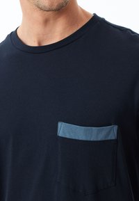 Camiseta de algodón azul marino con un bolsillo de un azul claro contrastante. Presenta un escote redondo y mangas cortas, con una textura suave en toda su superficie.