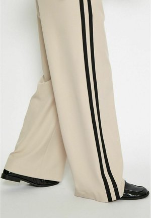 Beige wide-leg pants featuring black side stripes. Made of smooth fabric, they have pockets and are paired with shiny black footwear.