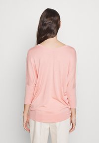 Pull en tricot doux rose clair, avec un col en V, des manches trois-quarts et une coupe détendue. Design simple sans motifs ni ornements.