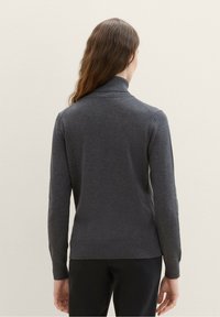 Grauer Strickpullover mit hohem Kragen, tailliertem Schnitt, langen Ärmeln und geripptem Saum. Glatte Textur ohne sichtbare Muster oder Hardware-Details.