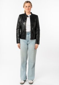 Zwart leren jas met een hoge kraag, ritsluiting en slim fit, gecombineerd met hoog - taille lichtblauwe jeans en grijze sneakers.