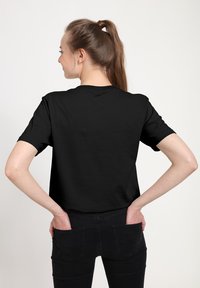 Czarny bawełniany t-shirt z klasycznym okrągłym dekoltem, krótkimi rękawami i luźnym krojem. Noszony z ciemnymi dżinsami; gładka tekstura, minimalistyczny design.
