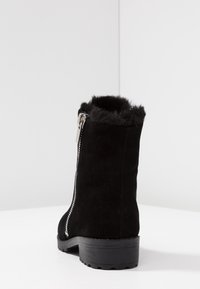 Bottine en daim noir avec une bordure en fausse fourrure texturée, une fermeture éclair latérale et une semelle en caoutchouc noire robuste. Présente un design élégant et minimaliste.