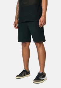 Shorts en coton noirs à coupe droite, associés à un t-shirt en mesh noir et des chaussures noires et olive avec des accents blancs.