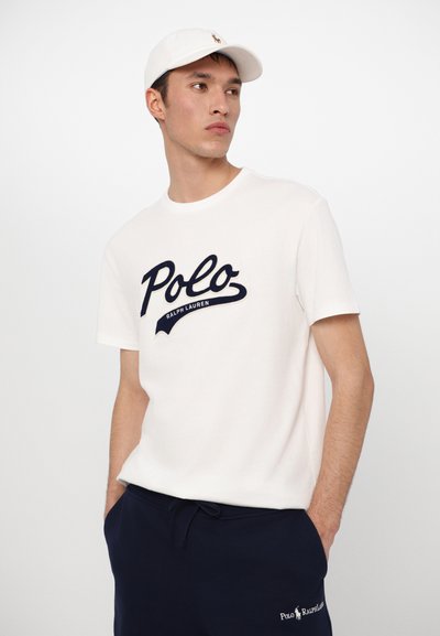 T-shirt de algodão branca com um logótipo bordado em azul-marinho "Polo" e "Ralph Lauren" por baixo, combinado com calças de moletom em azul-marinho.