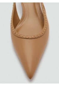 Bailarina de punta afilada en cuero color tostado, con una textura suave y acentos de tachuelas doradas a lo largo del borde ondulado. Diseño minimalista.