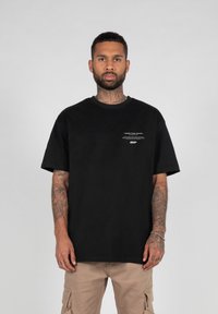 Black cotton t-shirt with short sleeves, round neck, featuring white text on the front. Paired with beige cargo pants.