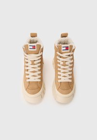 Sneaker alte color talpa in suede con interno in materiali morbidi, caratterizzate da lacci beige e una spessa suola bianca. Logo Tommy Jeans sulla linguetta.