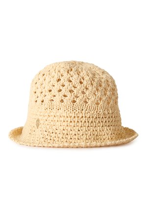 Béžový háčkovaný klobouk v provázkovém vzoru s volným pletením a malým kulatým kovovým logem na boku, zobrazený na bílém pozadí.