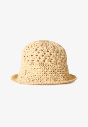 Beżowy szydełkowany kapelusz typu bucket z luźnym, otwartym wzorem dzianiny i małym, okrągłym metalowym logo po boku, pokazany na białym tle.