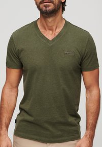 T-shirt verde oliva a V in morbido cotone con maniche corte. Presenta un logo ricamato discreto sul petto.