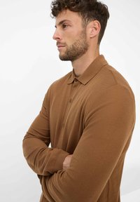 Bruine lange mouwen polo shirt met een gestructureerd breipatroon, knoopsluiting en kraag, gezien vanaf de zijkant tegen een witte achtergrond.
