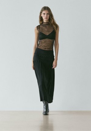 Průsvitný černý top s žebrovanou texturou a vysokým výstřihem, doplněný černou plisovanou maxi sukní a černými kozačkami po kolena.