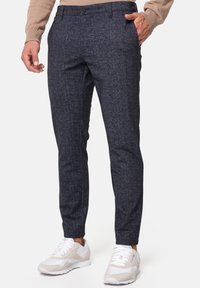 Pantalons texturés marine à coupe ajustée, dotés d'une fermeture à bouton et de poches latérales, associés à des baskets blanches et gris clair.