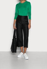 Vihreä neule, mustat cropped-housut, joissa on lahje, valkoiset platform-urheilukengät ja musta olkalaukku. Materiaalit vaihtelevat tekstuuriltaan.