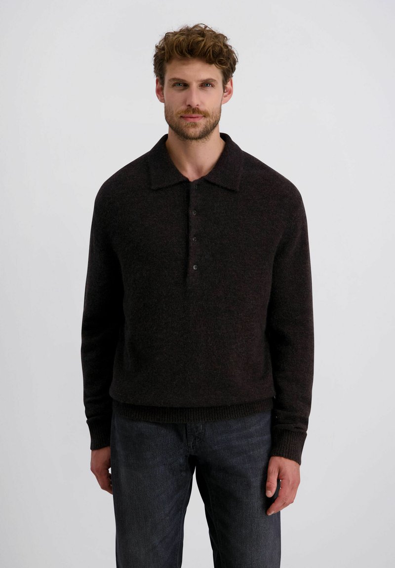 Dunkelbrauner Strickpullover mit Kragen, einer Knopfleiste mit drei Knöpfen und gerippten Bündchen, kombiniert mit dunklen Jeans.