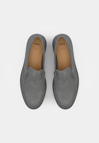 Zapatillas de ante gris de tipo slip-on con costuras, suela de goma y forro interior beige. Logotipo de la marca visible en el tacón y en el interior.