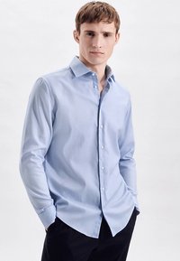 Lichtblauw overhemd met lange mouwen gemaakt van zachte stof, voorzien van een button-down kraag en een rechte zoom, gedragen met een donkere broek.