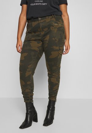Person wearing green and brown camouflage cargo pants with side pockets and black heeled ankle boots.