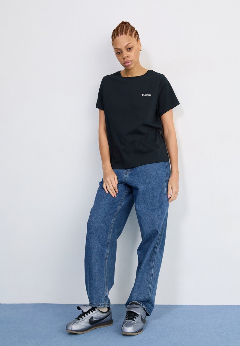 Schwarzes T-Shirt mit kurzen Ärmeln und kleinem Logo, kombiniert mit hellblauen, weit geschnittenen Jeans und grauen Sneakers. Schlichtes Design und lässiger Stil.