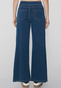 Pantalones de mezclilla de pierna ancha en azul oscuro, con una alta cintura, dos bolsillo traseros y una textura suave. Terminados con costuras en contraste.