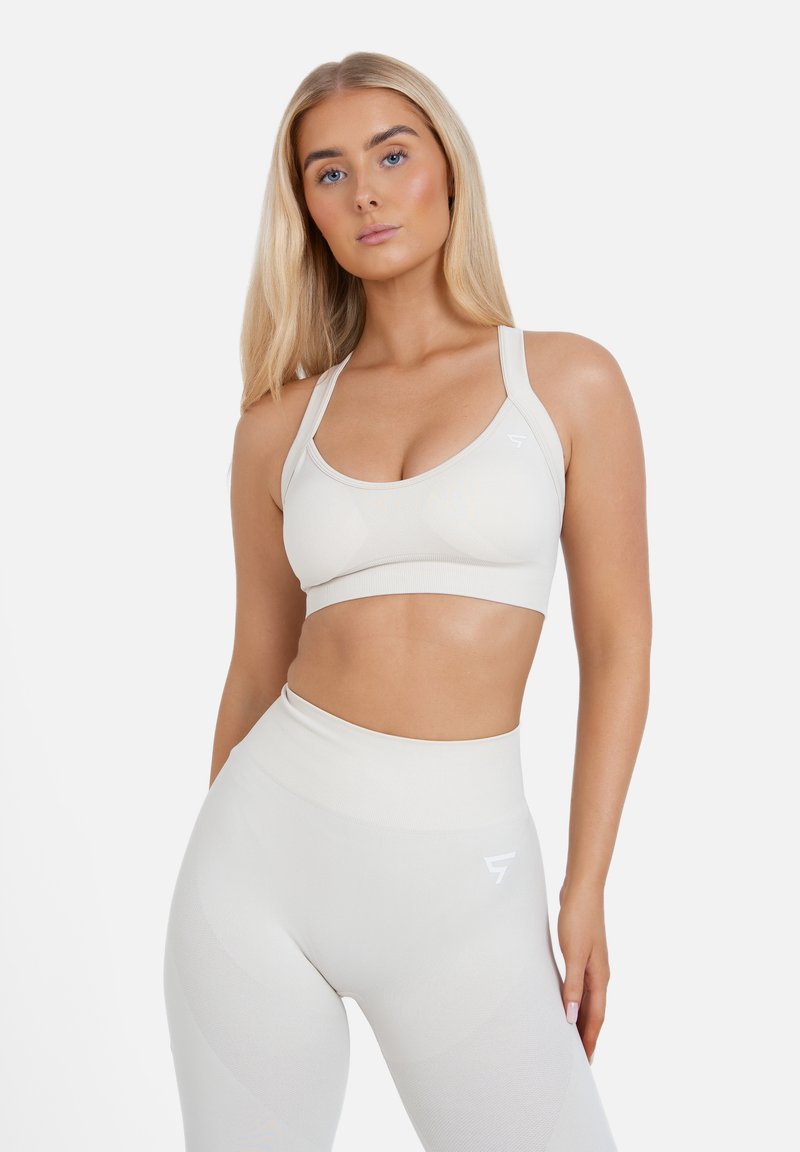 Lichtbeige sportbeha en hoge taille legging met een gestructureerd, geribbeld patroon. Beide hebben minimale merkvermelding en een aansluitend ontwerp voor comfort.
