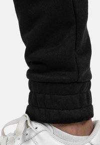 Zwarte joggers met een strakke, omgeslagen zoom, gemaakt van zachte stof. Gecombineerd met een witte sneaker met veters en een gestructureerde zool.