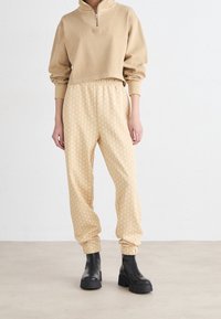 Beige cropped sweatshirt met halve ritssluiting, gecombineerd met beige gestreepte elastische broek en zwarte enkellaarzen. Glad stofgevoel.