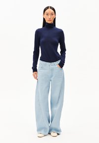 Navyblaues Rollkragenoberteil kombiniert mit hellblauen, hoch taillierten, weiten Jeans. Das Outfit zeichnet sich durch einen glatten Stoff und eine lockere Passform aus.