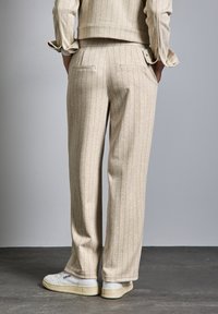 Beige rutiga byxor som är gjorda av mjukt material, med en avslappnad passform och två bakfickor. Matchas med vita sneakers.