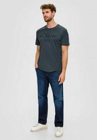 Dark gray t-shirt with a crew neck and short sleeves, featuring black printed text. Paired with dark blue jeans and white sneakers.