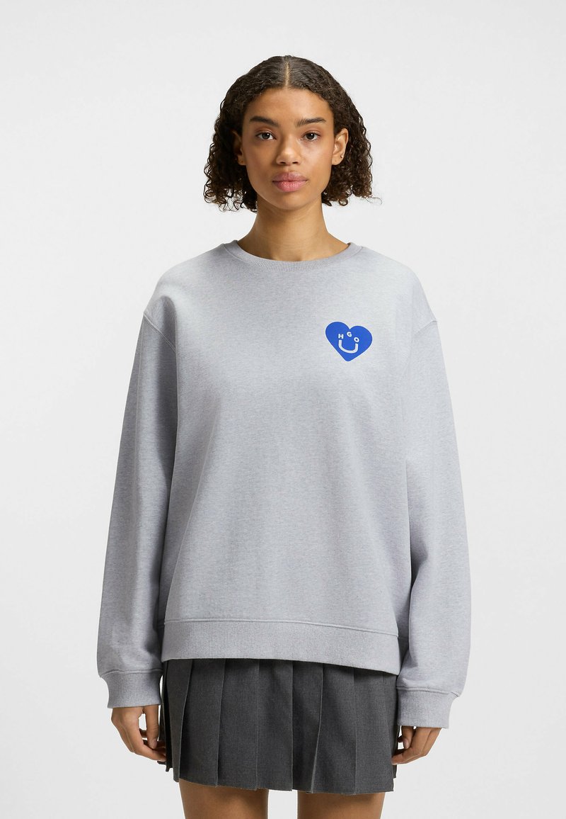 Grijze sweatshirt met een blauw hartvormig logo op de linkerkant van de borst. Losse fit met lange mouwen en geribde manchetten. Zachte, gestructureerde stof.