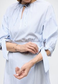 Φόρεμα με γαλάζιες και λευκές ρίγες, ντεκολτέ σε σχήμα κλειδαρότρυπας, φαρδιά μανίκια δεμένα στους καρπούς και λείο, ρέον ύφασμα.