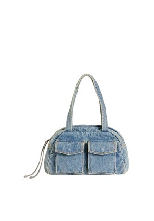 Blå denim håndtaske med to frontklaplommer, dobbelt håndtag og en sidelomme med lynlås på en hvid baggrund.