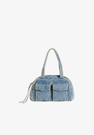 Blå denim håndtaske med to frontklaplommer, dobbelt håndtag og en sidelomme med lynlås på en hvid baggrund.