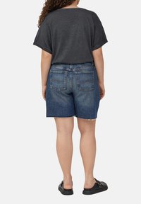 Haut gris à manches courtes avec un large col, associé à un short en denim bleu avec des bords effilochés et deux poches arrière. Chaussures noires visibles.