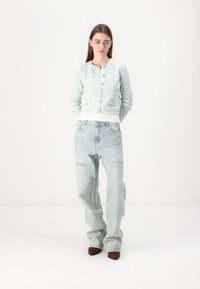 Light green textured cardigan with round neckline and silver buttons, paired with loose light blue jeans and brown pointed-toe shoes.