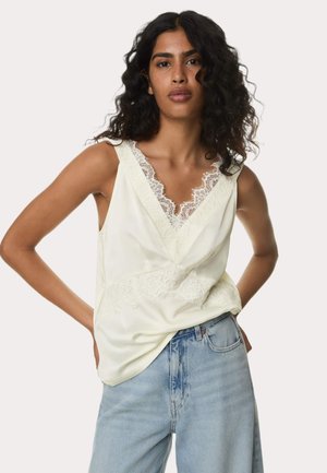 Soft yellow sleeveless top with lace trim along the neckline and waist, paired with light blue denim jeans, showcasing a relaxed fit.