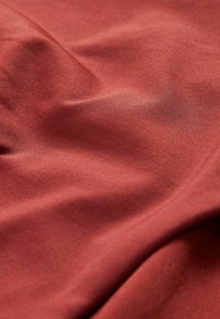 Röd tyg med en slät, något glänsande texture, som har fina horisontella räfflor och mjuka draperingar, som visar subtila ljusreflektioner.