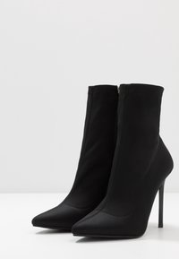 Stivali ankle neri realizzati in tessuto morbido, con punta affilata, alto tacco a stiletto e una cerniera laterale per una facile vestibilità.