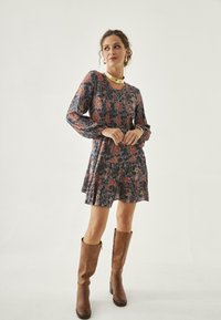 Vestido de manga larga hasta la rodilla con un patrón floral en tonos rosa y azul, hecho de tela ligera. Botas marrones hasta la rodilla.