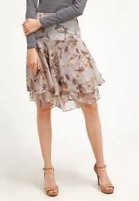 Kukkakuvioinen kerroshame vaaleanbeigessä, ruskeilla yksityiskohdilla. Pehmeä, läpikuultava kangas luo liehuvan siluetin. Yhdistetty ruskeisiin korkeakorkoisiin sandaaleihin.