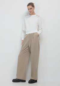 Felpa bianca con dettagli in pizzo sulle spalle e nei polsini, abbinata a pantaloni a gamba larga color beige e scarpe con platform nere. Design minimalista.